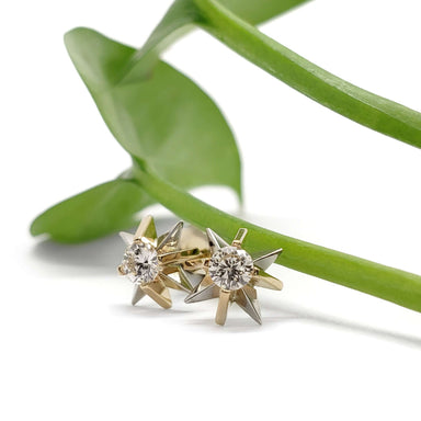 Vintage diamond starburst earrings in 14kt yellow and white gold displayed with green leaf