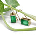 Vintage emerald dangle earrings in 14kt yellow gold displayed with green plant