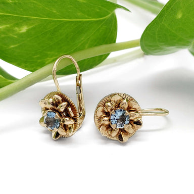 Vintage 14kt yellow gold lotus earrings with blue topaz, displayed with green leaves