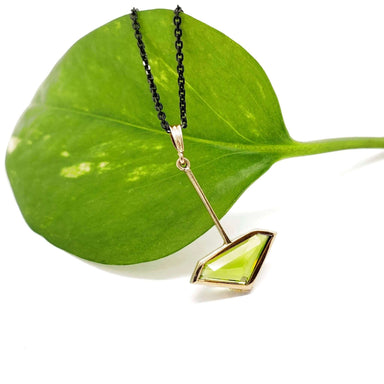 Vintage peridot pendant in 14kt yellow gold displayed on green leaf