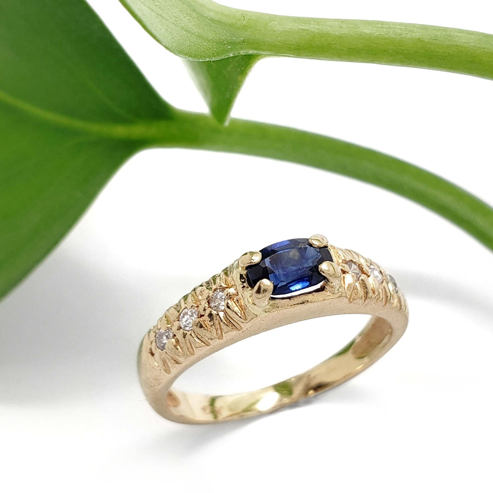 Vintage sapphire and diamond pinky ring in yellow gold beside a green leaf