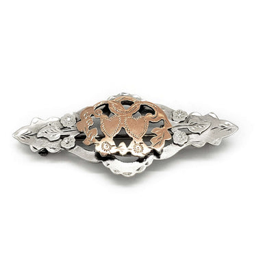 Vintage silver and rose gold pin with double heart, leaf, and flower motif on white background