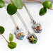 Three vintage silver crest pendants on chains with Venezia, Heidelberg, and Fiji Islands motifs, styled with greenery