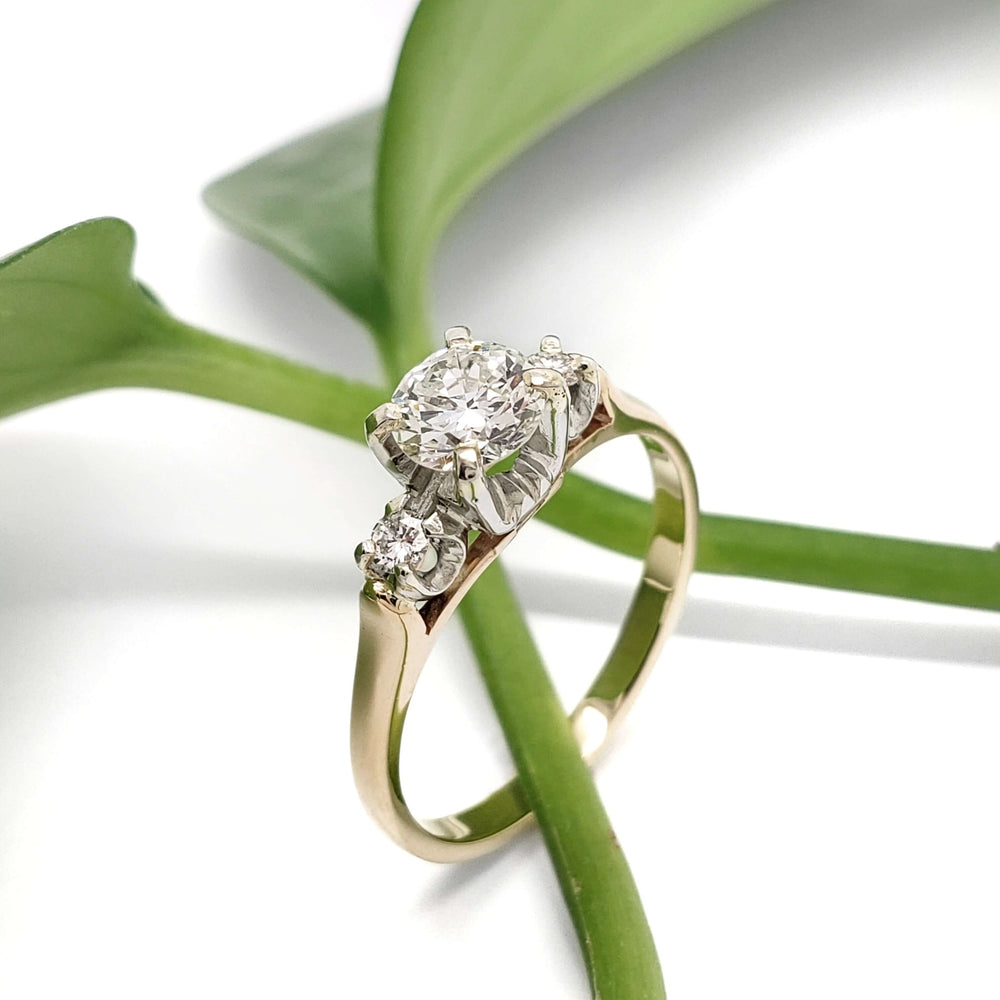Vintage three-stone diamond ring with yellow gold band and white gold setting, on leafy background