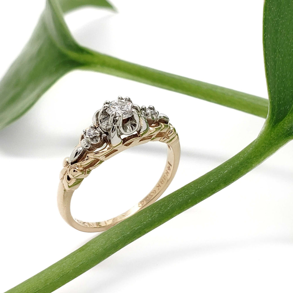 Vintage diamond ring in yellow and white gold displayed with green leaf