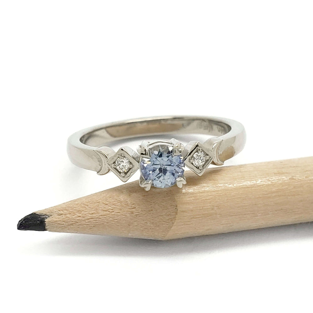 White gold ring with blue Montana sapphire and two diamonds, shown beside a pencil