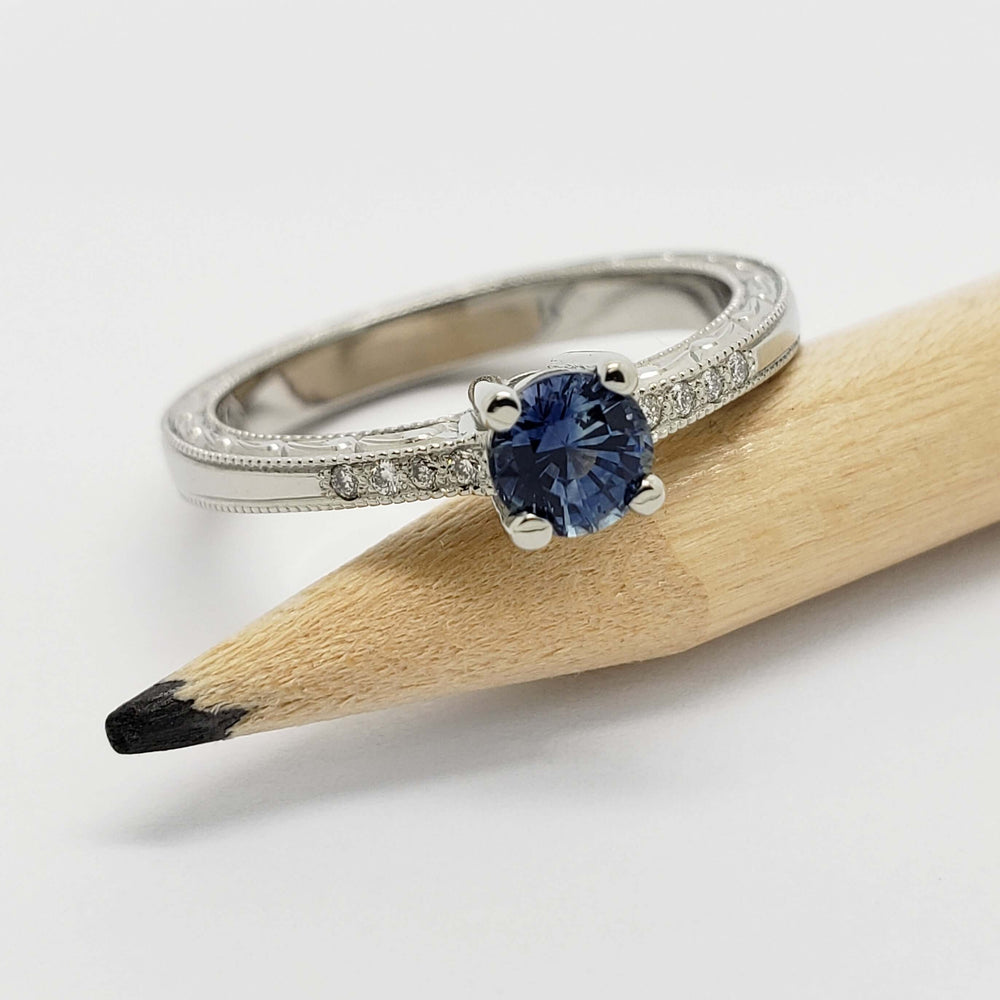 White gold ring with blue Montana sapphire and diamond accents, displayed on a pencil