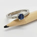 White gold ring with blue Montana sapphire and diamond accents, displayed on a pencil