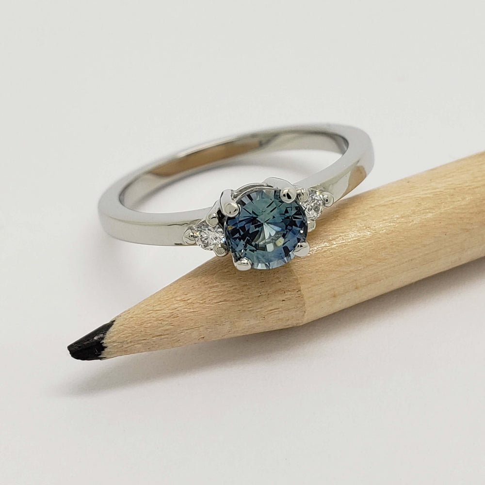 White gold ring with blue Montana sapphire and side diamonds, shown with pencil for scale