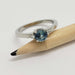White gold ring with blue Montana sapphire and side diamonds, shown with pencil for scale