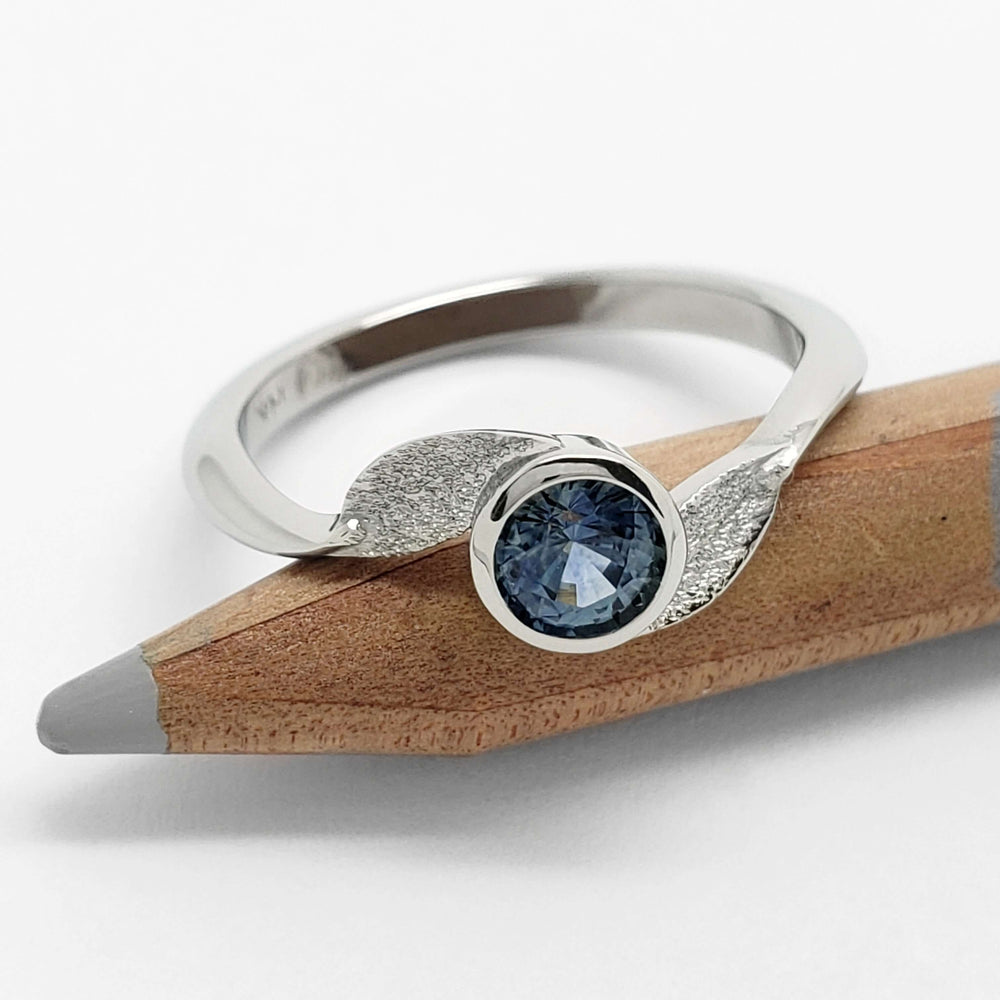 Bezel-set blue Montana sapphire ring in white gold resting on a pencil