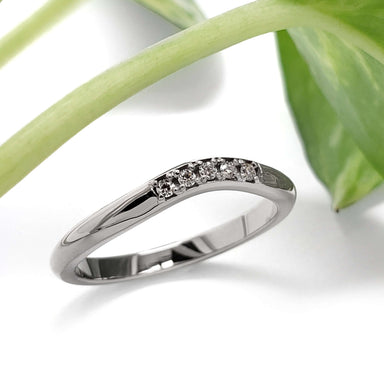White gold chevron diamond wedding ring beside a green leaf
