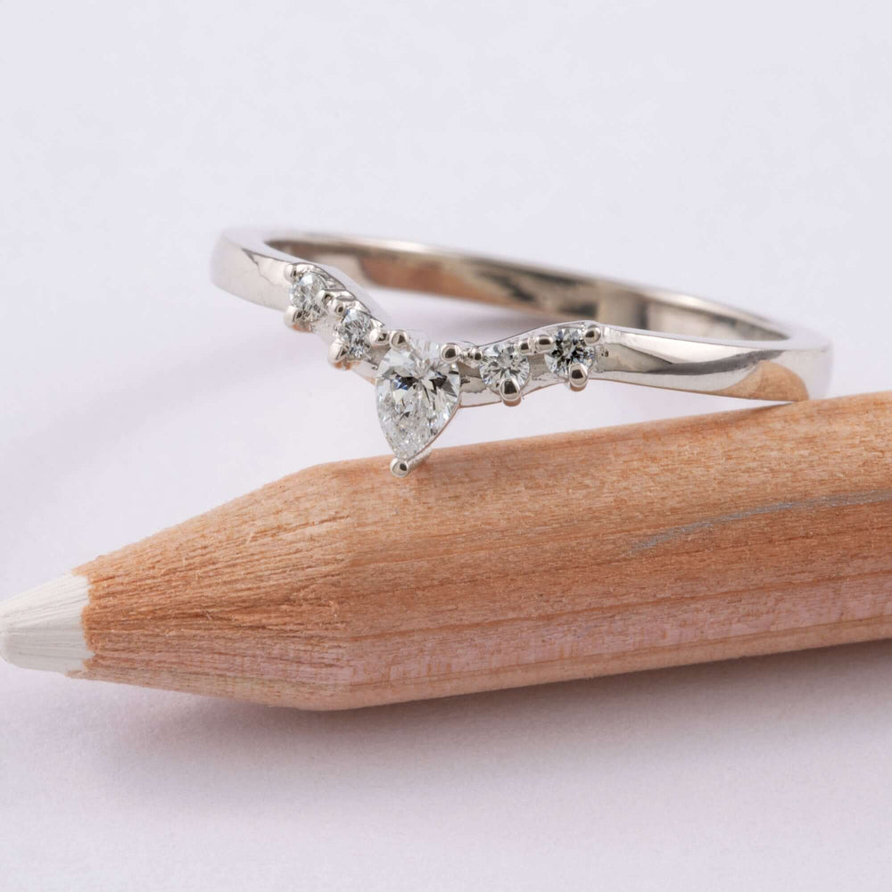 White gold chevron wedding ring with pear cut diamond and round diamonds on a pencil