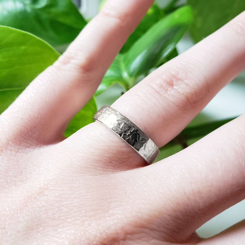 Textured white gold wedding band worn on hand, close-up