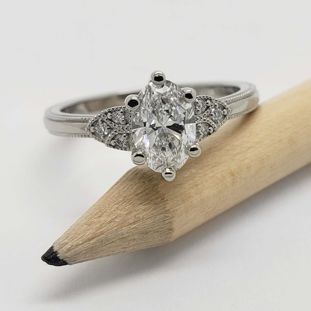 White gold engagement ring with oval lab grown diamond and pave-set side stones, shown with pencil