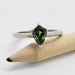 White gold engagement ring with shield cut green sapphire resting on a pencil