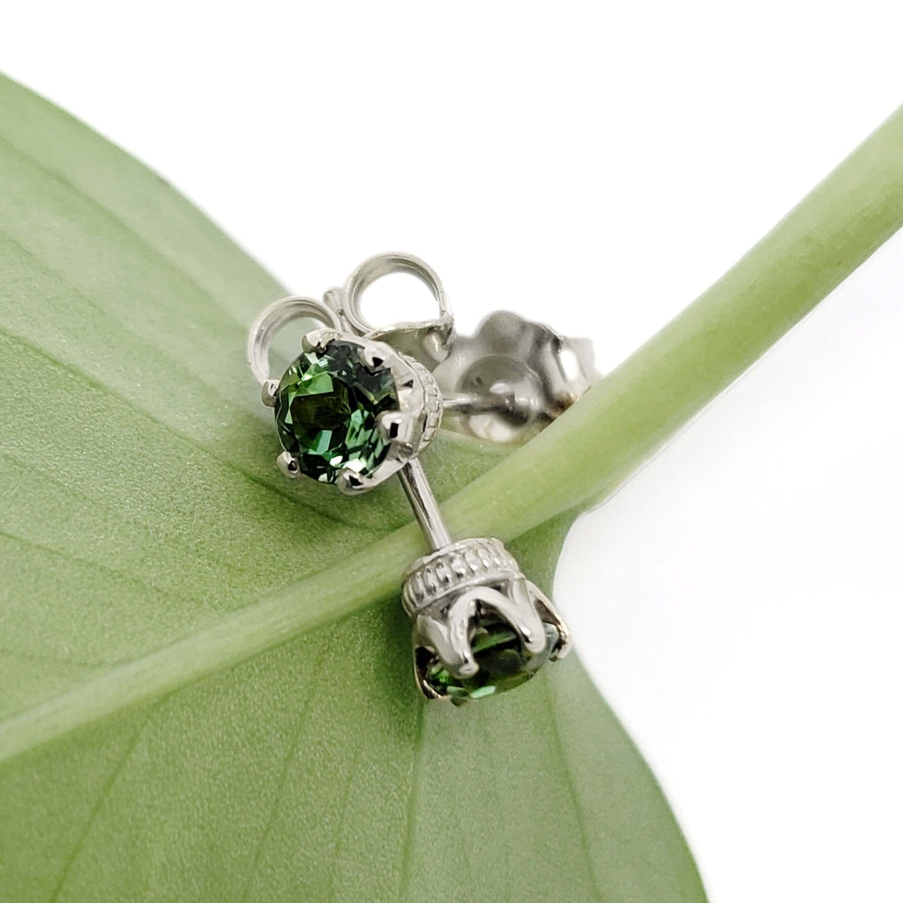 Close-up of green tourmaline stud earrings in white gold crown settings on a leaf