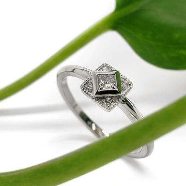 White gold lab diamond engagement ring with vintage-inspired millgrain beside a green leaf