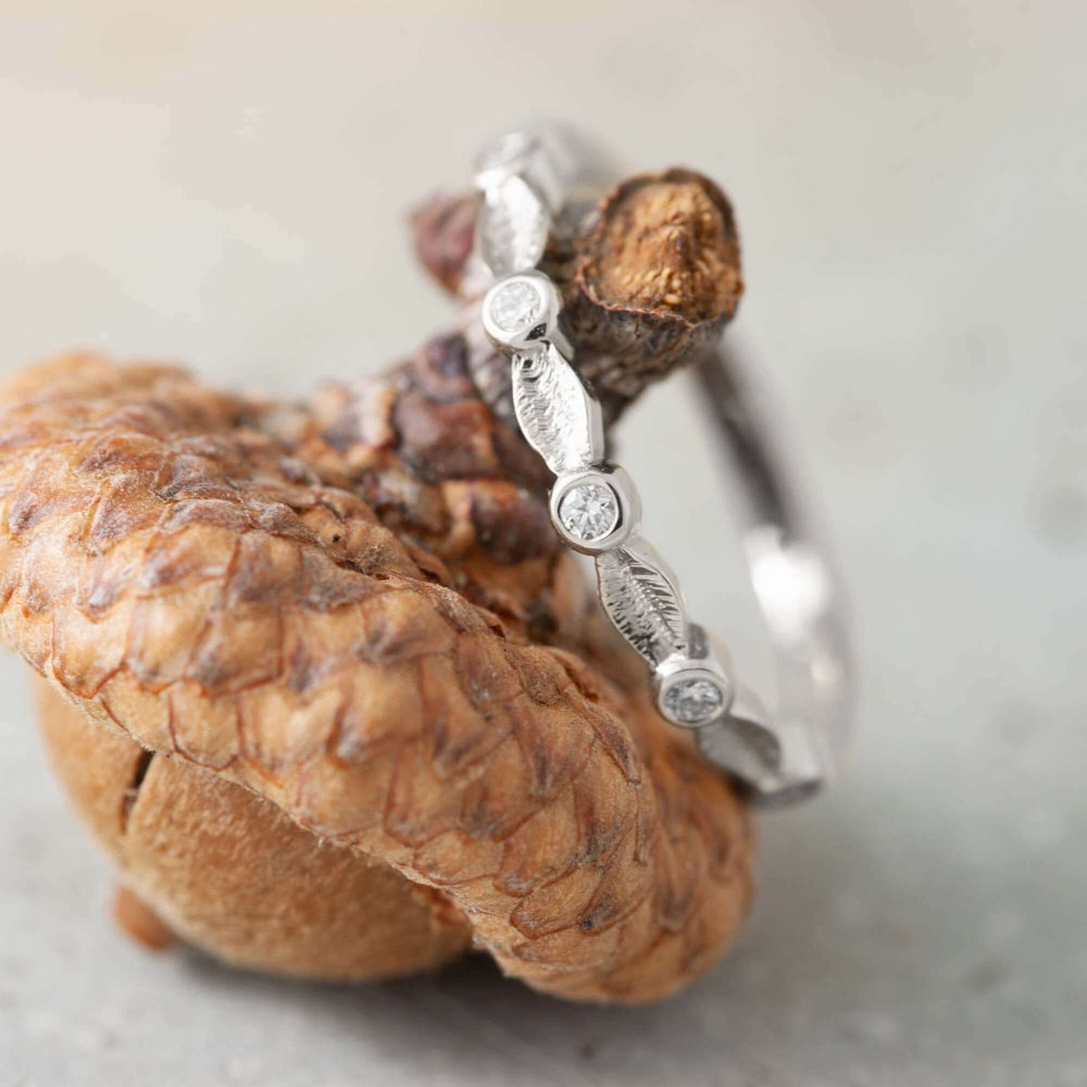 Handcrafted white gold leaf and diamond wedding ring resting on an acorn