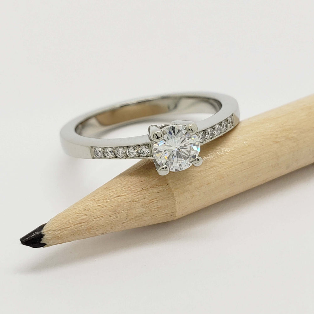 White gold moissanite and lab diamond ring displayed on a pencil