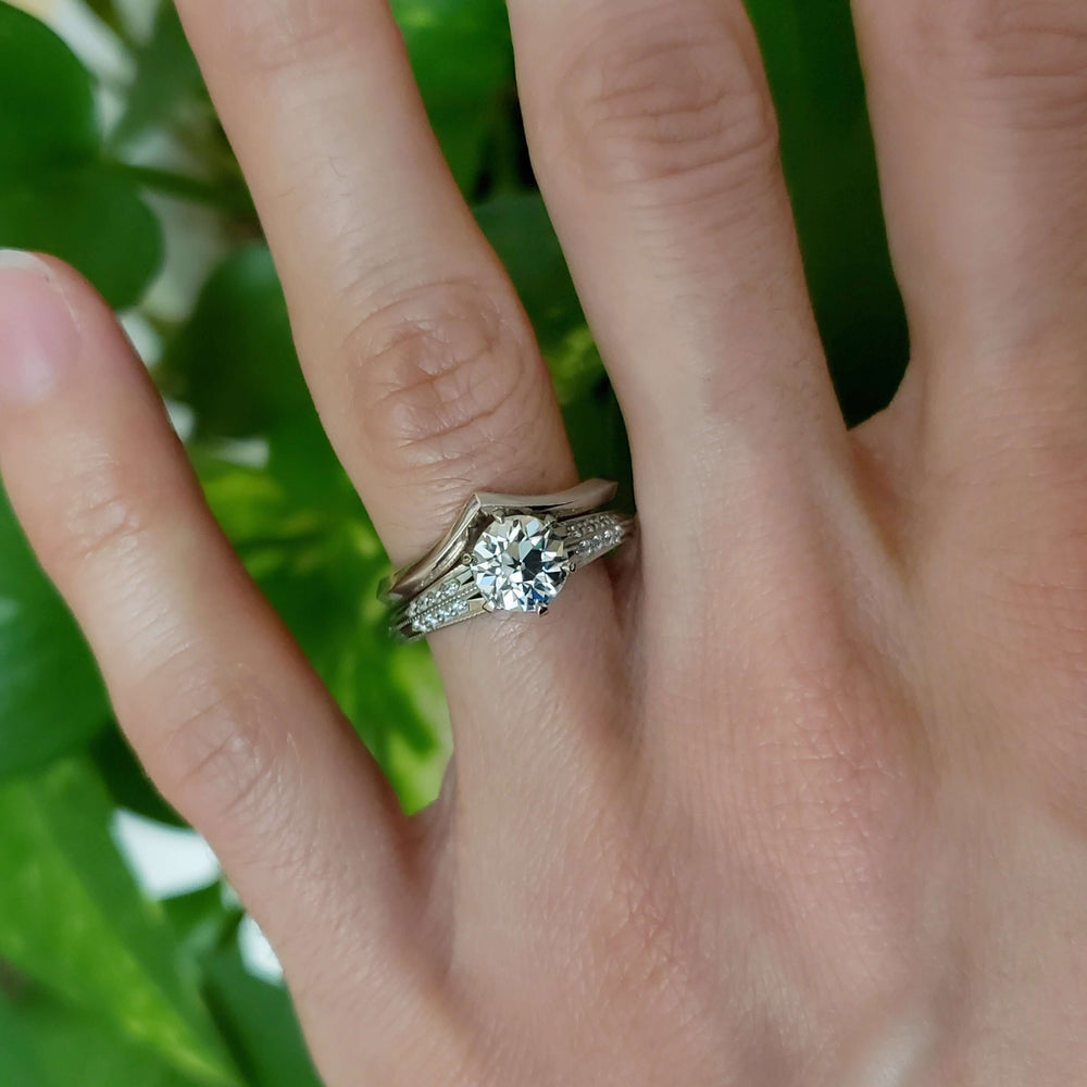 White gold moissanite engagement ring with diamond accents, paired with a wedding band on hand