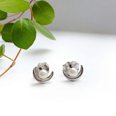 14k white gold pearl moon stud earrings displayed on white surface with green leaves