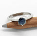 White gold ring with blue round Montana sapphire resting on a pencil