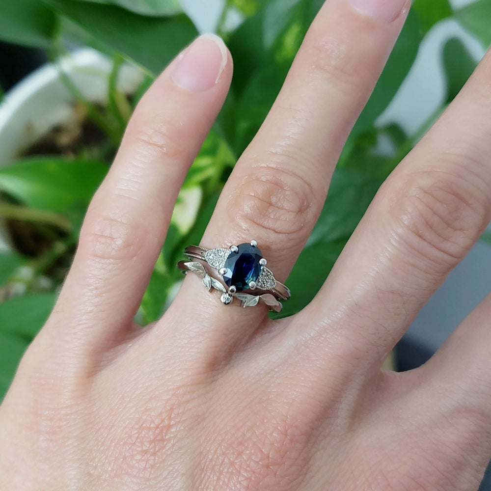White gold sapphire and diamond engagement ring stacked with leaf-inspired band on hand