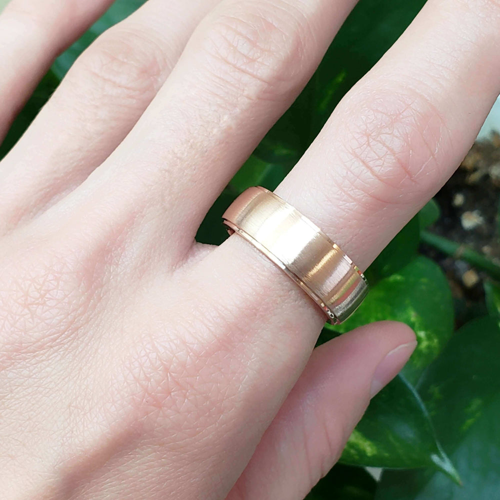 Wide 14kt rose gold wedding band with brushed finish shown on a hand