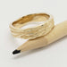 Woodgrain textured 14kt yellow gold ring beside a pencil for scale
