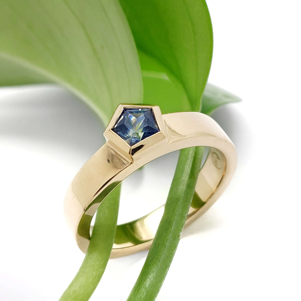 Yellow gold Montana sapphire ring displayed with green leaves