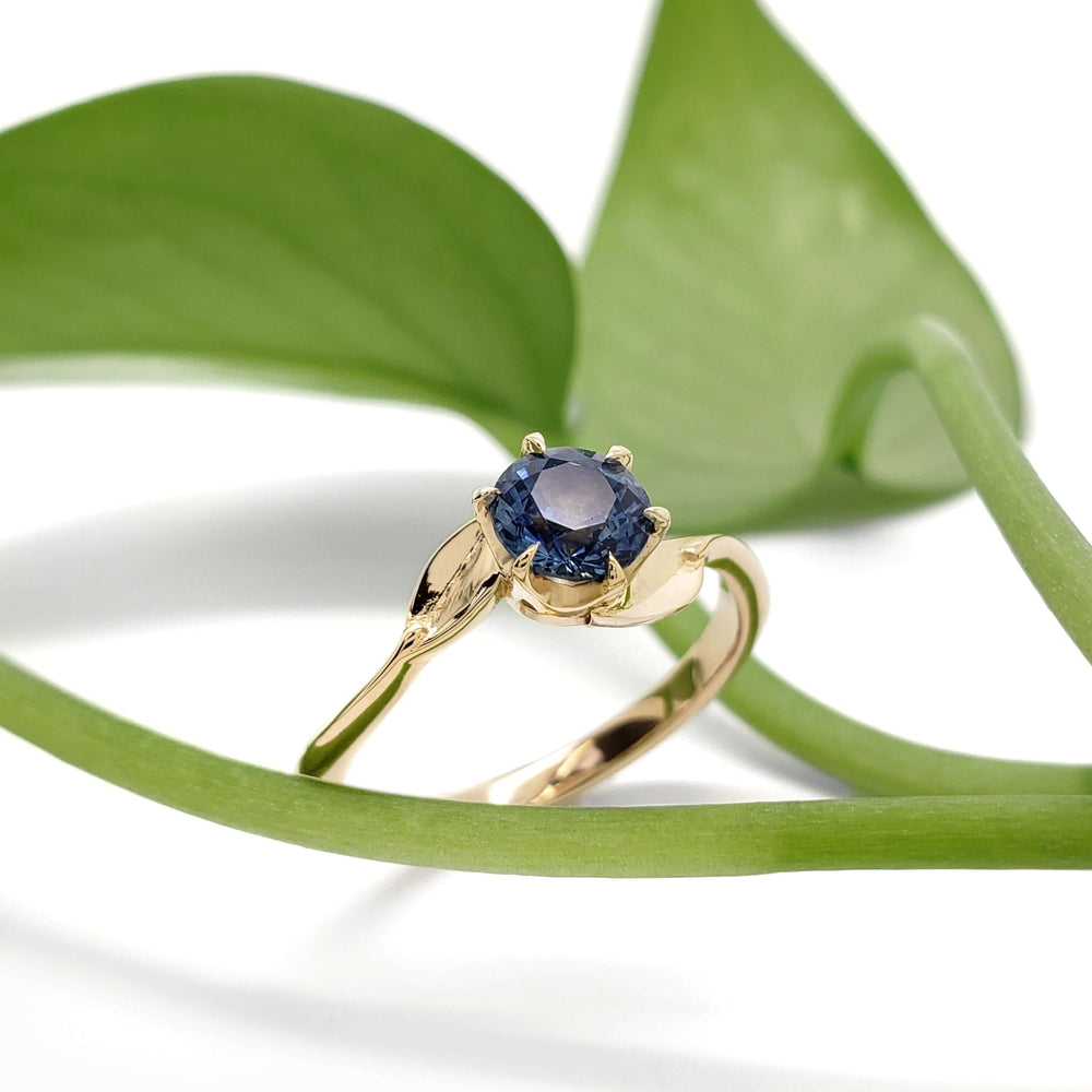Yellow gold Montana sapphire ring with leaf motif, styled with green plant