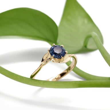 Yellow gold Montana sapphire ring with leaf motif, styled with green plant