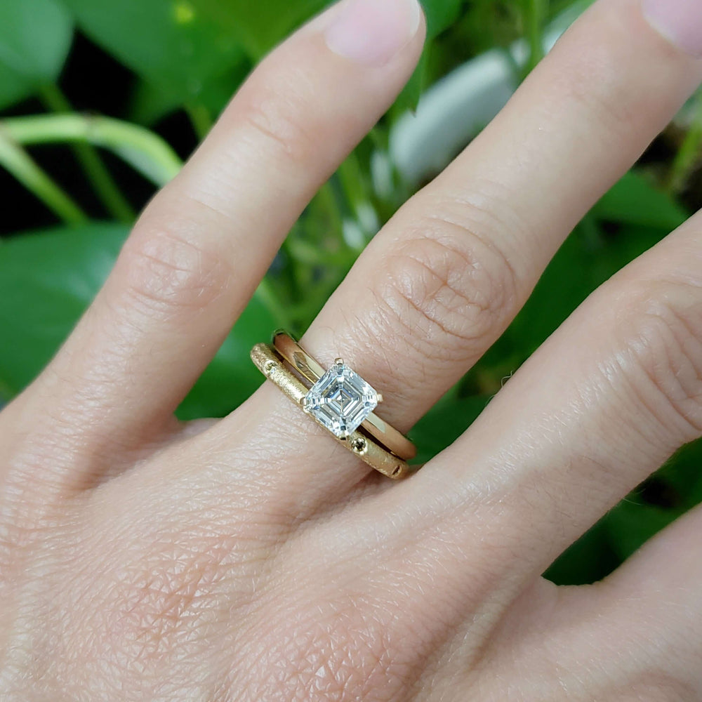 Yellow gold asscher cut lab diamond engagement ring stacked with gold band on hand