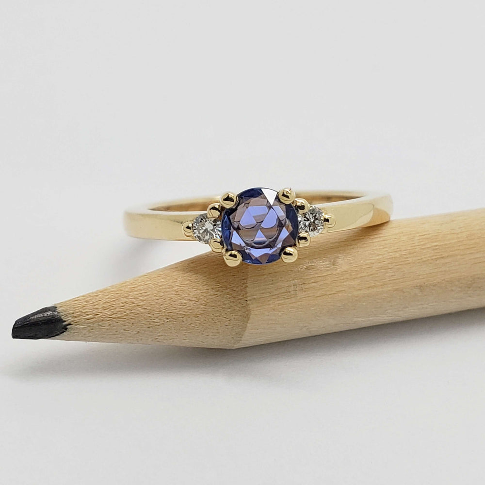 Yellow gold ring with blue sapphire and diamonds shown beside a pencil