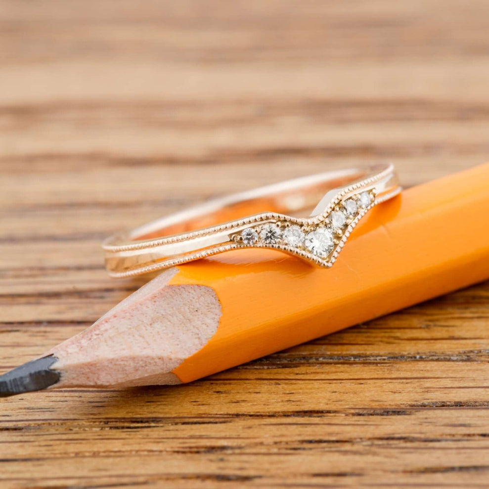 14k yellow gold chevron diamond wedding band resting on a pencil