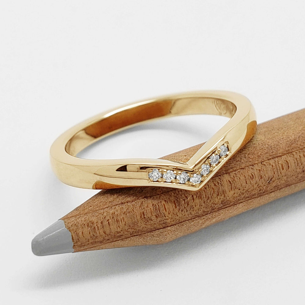 Yellow gold chevron diamond wedding ring displayed on a wooden pencil