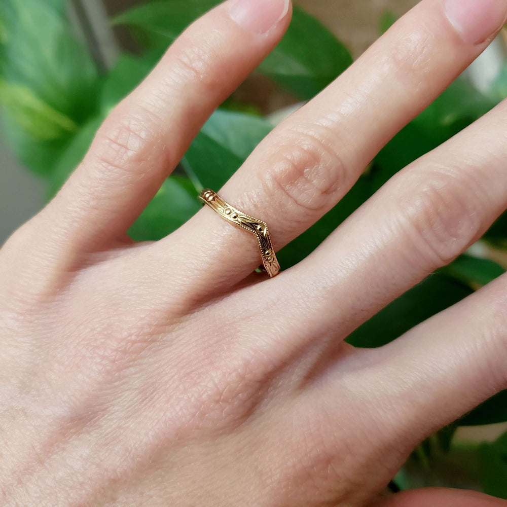 14kt yellow gold chevron wedding ring with berry engraving worn on a hand