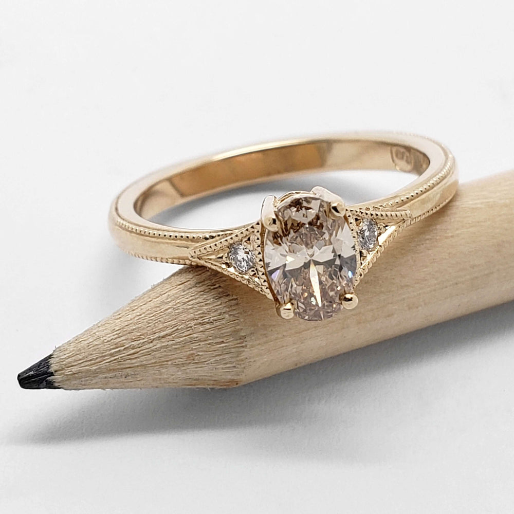 Yellow gold engagement ring with champagne oval diamond and Canadian diamonds, beside a pencil