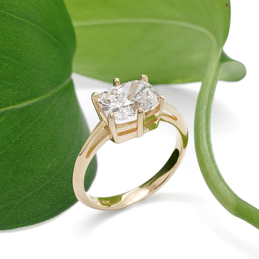 Handcrafted yellow gold engagement ring with cushion cut lab diamond beside green leaf