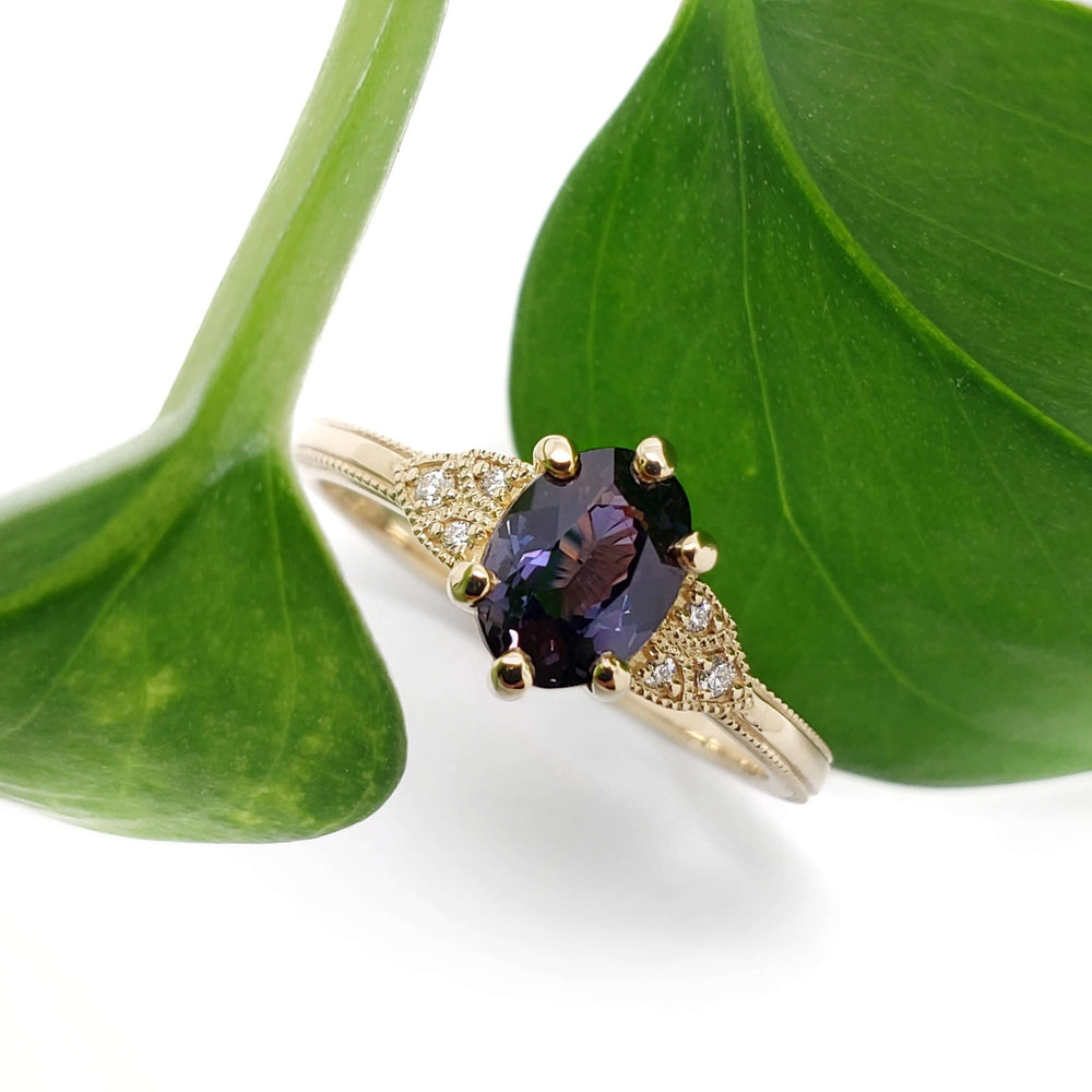 Yellow gold engagement ring with purple sapphire and diamond accents, shown with green leaves