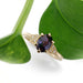Yellow gold engagement ring with purple sapphire and diamond accents, shown with green leaves