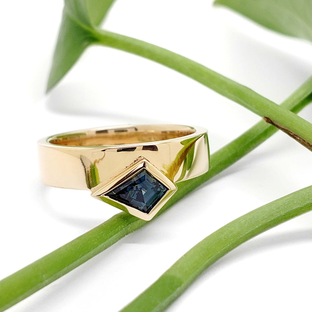 Yellow gold engagement ring with teal kite sapphire resting on green plant stems