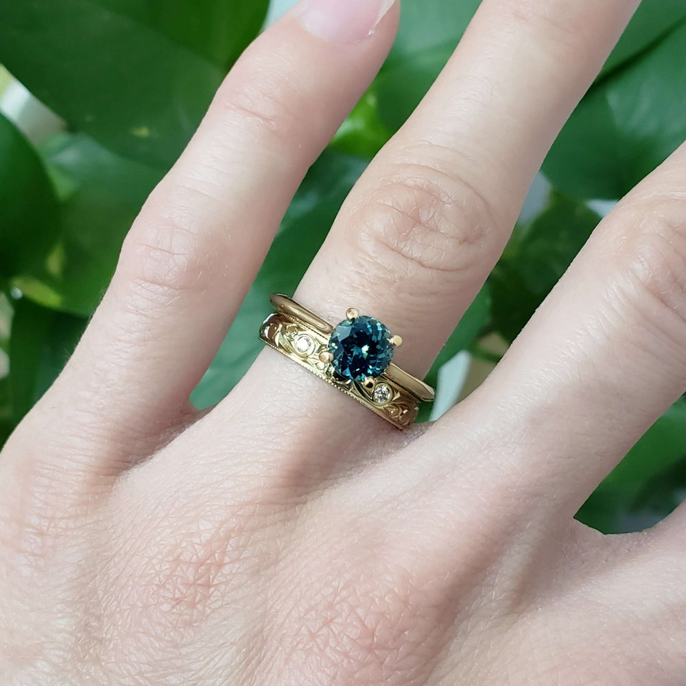 Yellow gold engraved diamond wedding band stacked with blue gemstone ring on hand