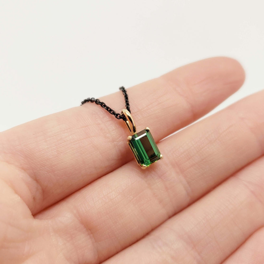 Emerald cut green tourmaline pendant in yellow gold on black chain shown on hand