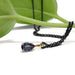 Lab alexandrite pear pendant in yellow gold with black chain, beside a green leaf