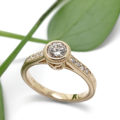 Yellow gold lab diamond engagement ring with engraved details, shown on white with leaf
