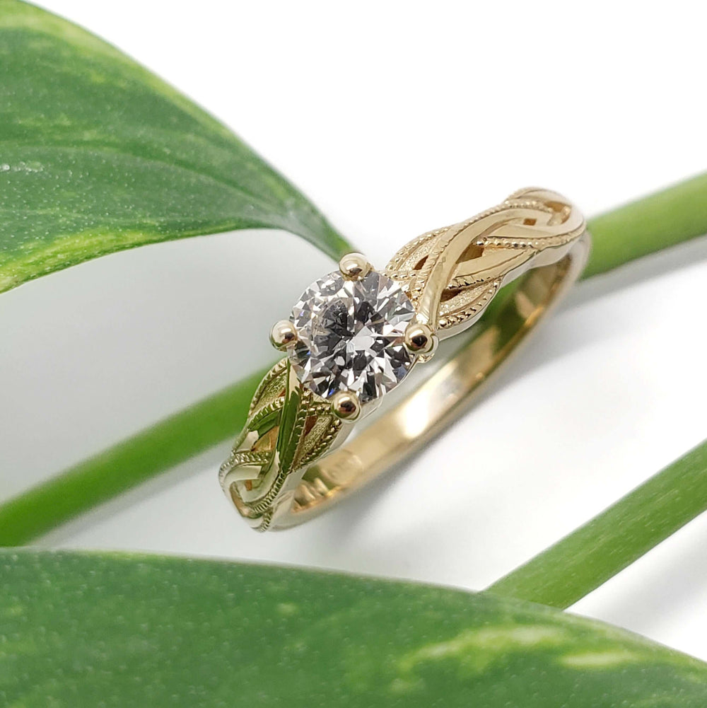 Yellow gold lab diamond engagement ring with intricate interlaced band, shown with green leaf