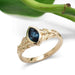 Handcrafted yellow gold ring with marquise blue sapphire, leafy detail, and plant background