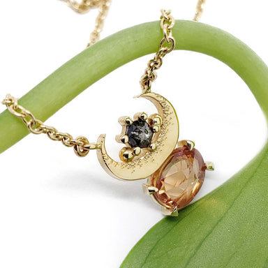 Crescent moon necklace in yellow gold with orange sapphire and salt and pepper diamond on a green stem
